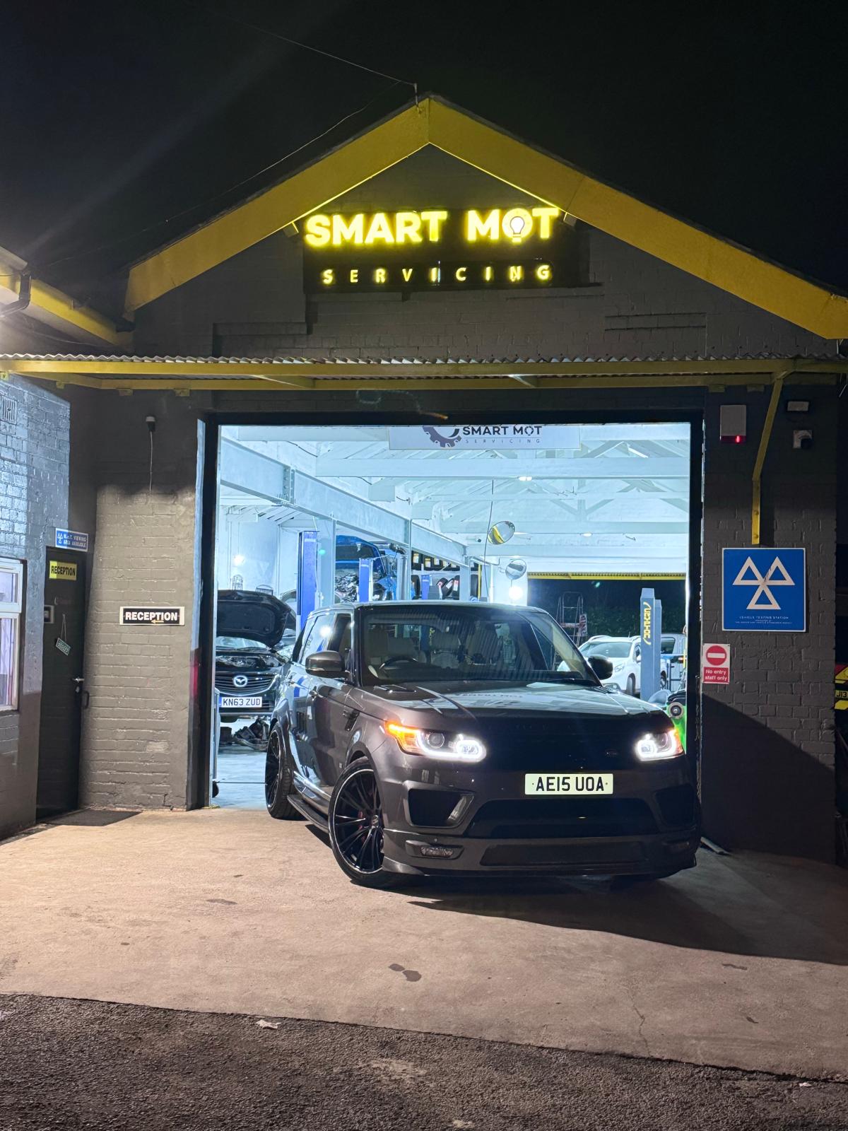 A car lit up in the Smart MOT & Servicing doorway at night